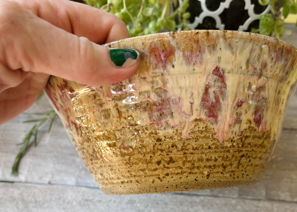 Side view of large handmade ceramic bowl showing sand and raspberry glaze exterior texture